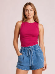 Model standing with one hand in the pocket of blue high-waist denim shorts, featuring a drawstring waist, relaxed silhouette, and cuffed hems.
