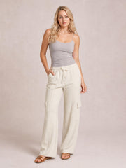 Model poses in cream high-waist drawstring pants with a wide-leg silhouette, side pockets, and flap cargo pockets, placing one hand in a pocket.