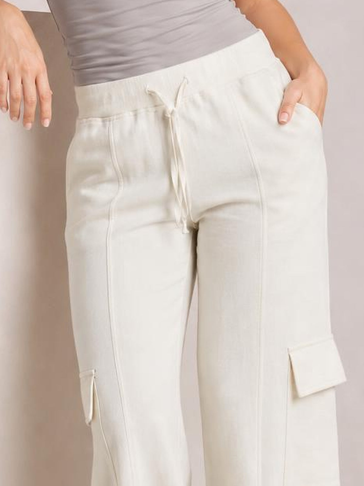 A model wears opaque white high-waist drawstring pants with a relaxed straight-leg silhouette, front pockets, and flap cargo-style side pockets.