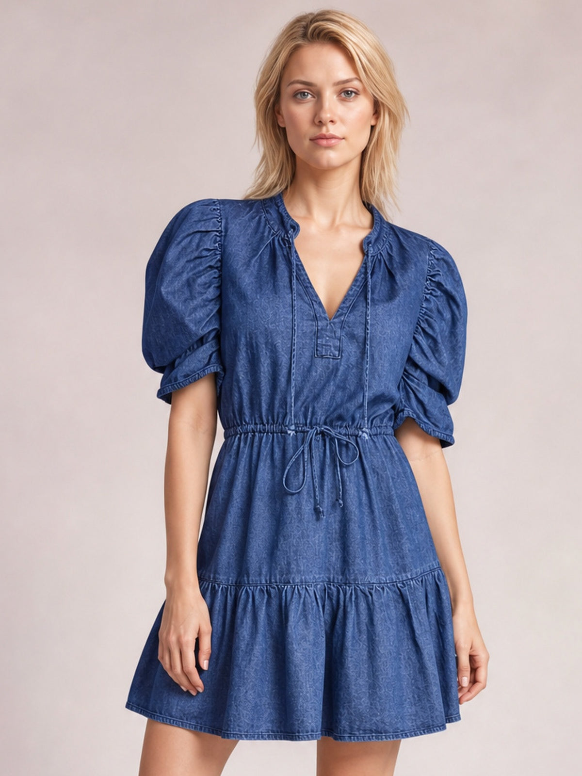 Model wears a navy denim mini dress with puff sleeves, V-neckline, drawstring high waist, and a gathered tiered skirt creating a feminine silhouette.