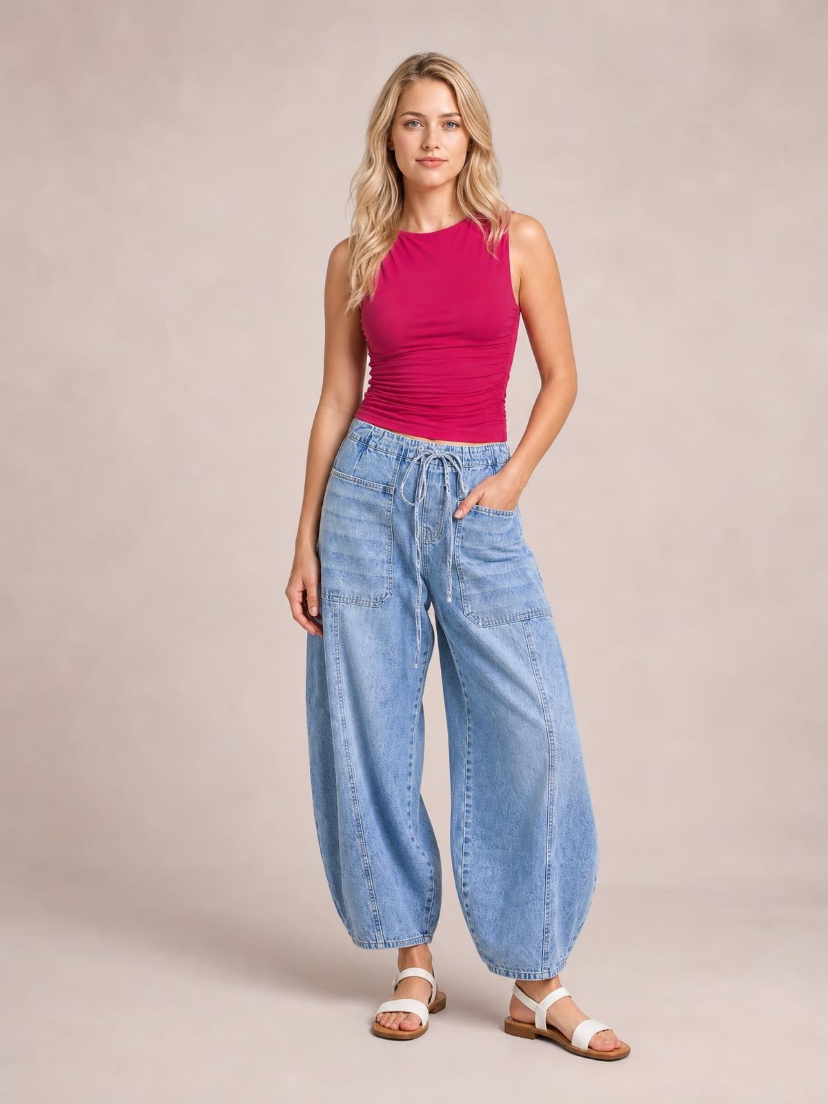 Model poses in light blue drawstring jeans with a relaxed wide-leg silhouette, elastic waist, visible tie, and practical patch pockets.