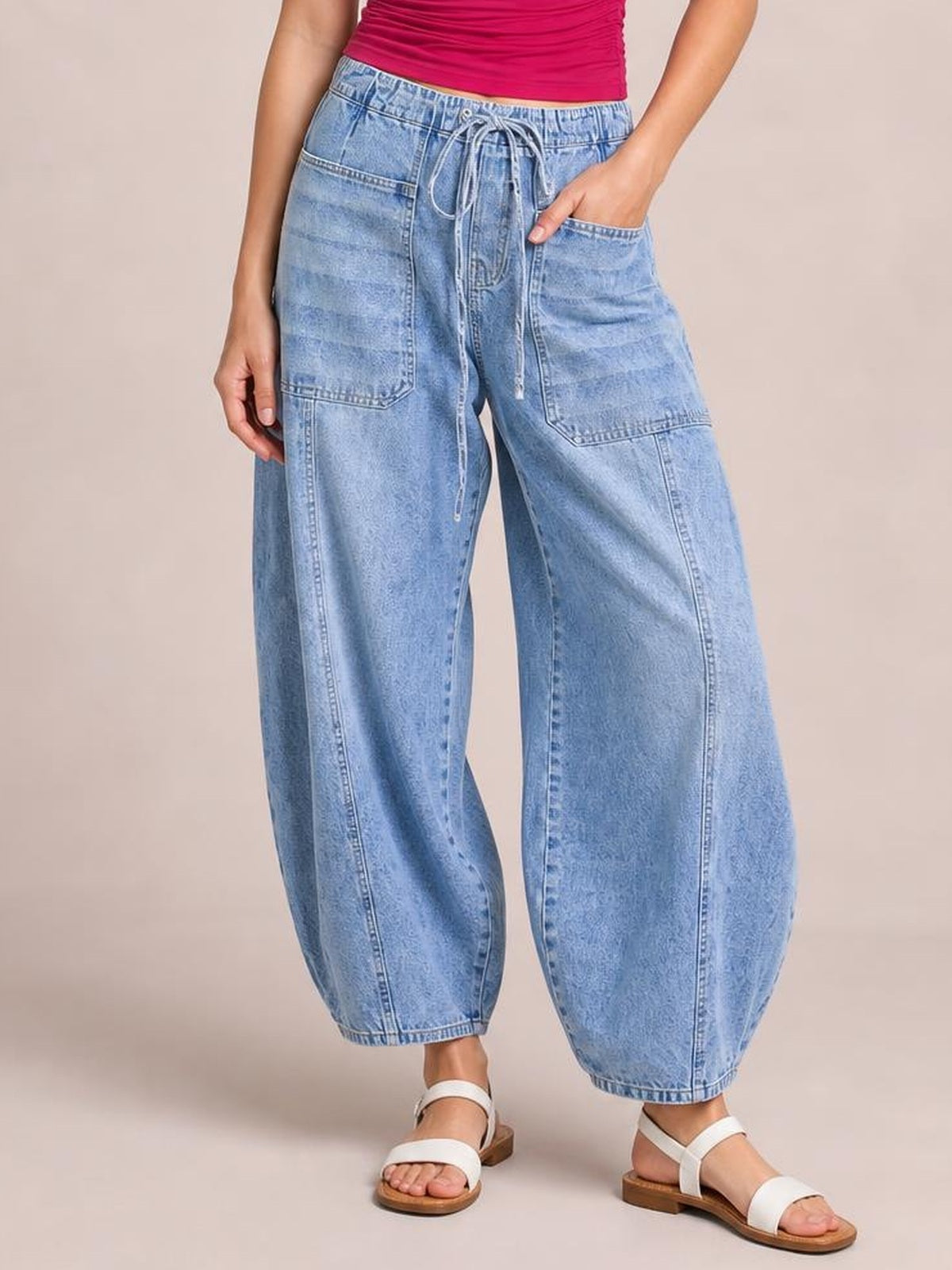 Model wears light-blue drawstring jeans with oversized patch pockets, a relaxed wide-leg silhouette, visible stitching, and ankle-length tapered hems.
