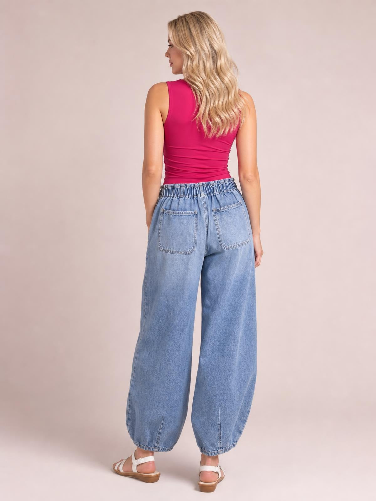 A model viewed from behind wears light blue drawstring jeans with an elastic waist, large back pockets, and a relaxed wide-leg silhouette with gathered hems.