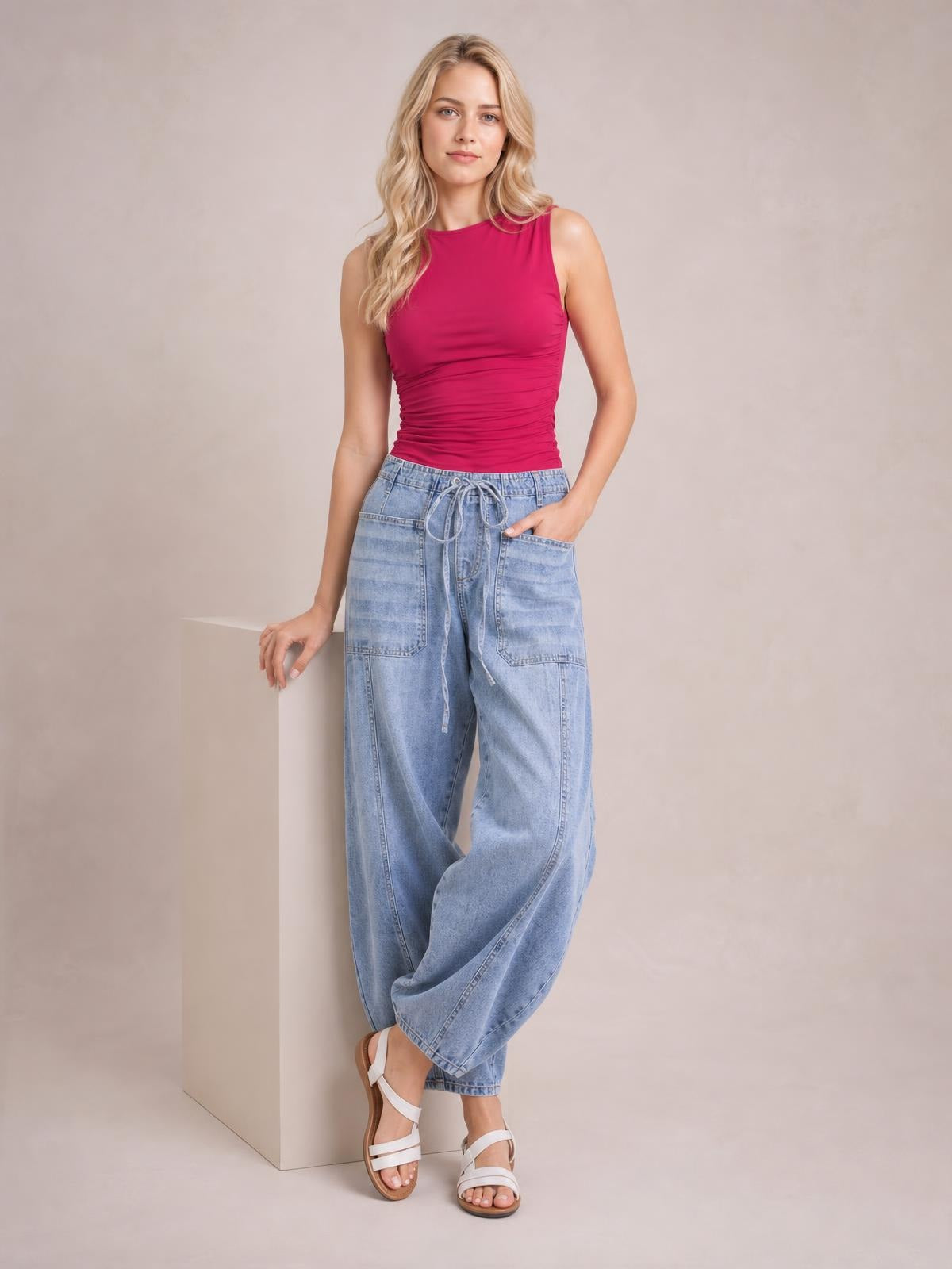 Model poses in light blue drawstring jeans with a relaxed wide-leg silhouette, front patch pockets, and a casual hand-in-pocket stance.