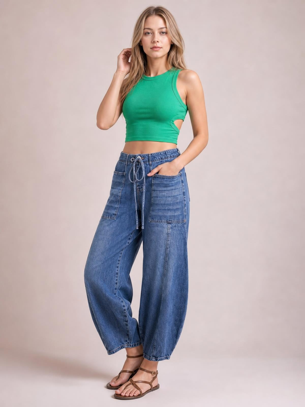 Model poses in blue drawstring jeans with large patch pockets, a relaxed wide-leg silhouette, elasticized waist, and ankle-length construction.