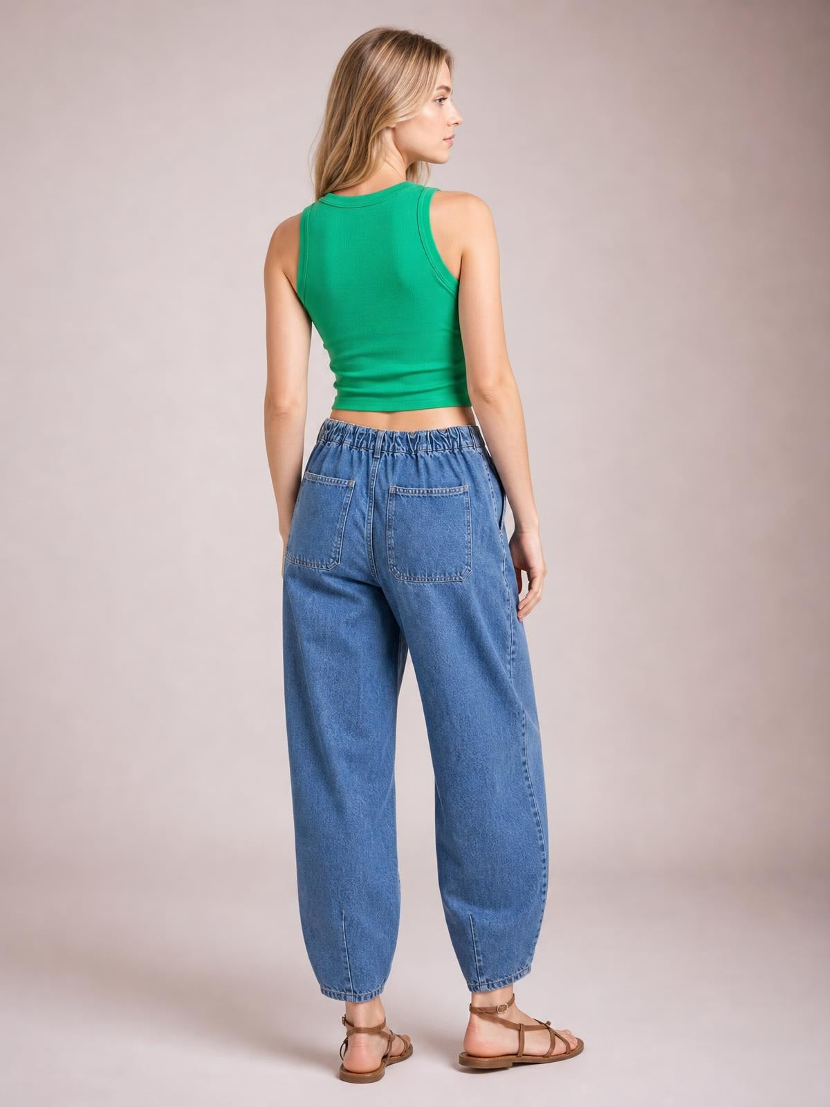 A model stands turned away in light-blue drawstring jeans with a gathered waistband, two back pockets, and a relaxed tapered silhouette ending at cropped cuffs.