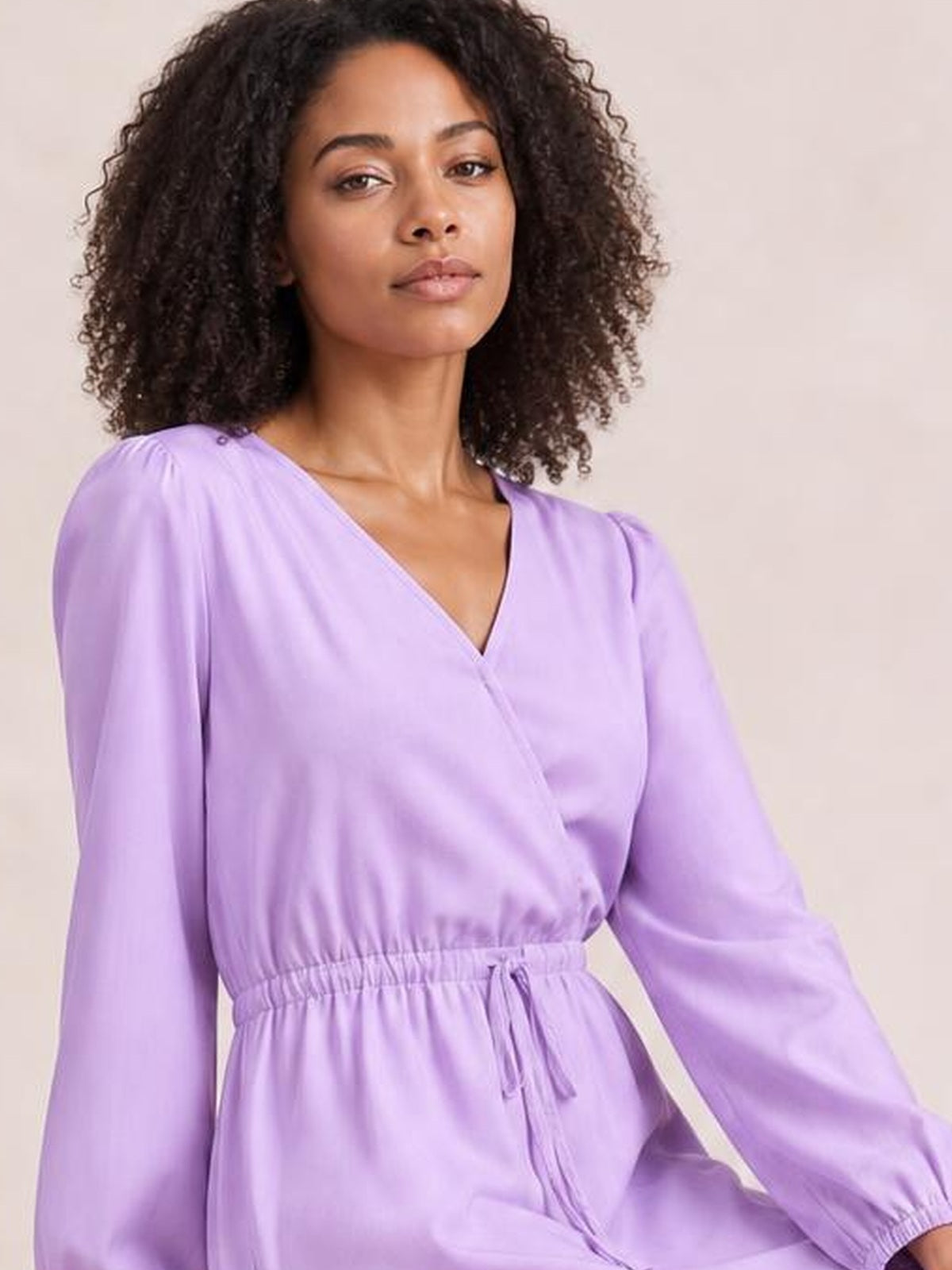 A model poses in a relaxed lavender long sleeve romper with a V-neck, elastic drawstring waist, and loose silhouette.