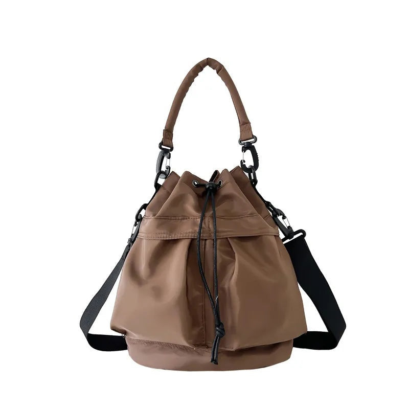 Medium brown nylon bucket bag with a softly gathered drawstring opening, top handle, adjustable side straps, and a structured base.