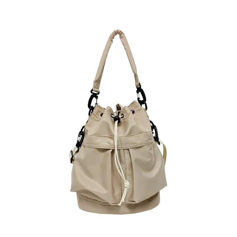 A medium beige nylon bucket bag with a softly gathered drawstring opening, adjustable straps, and a rounded structured base.