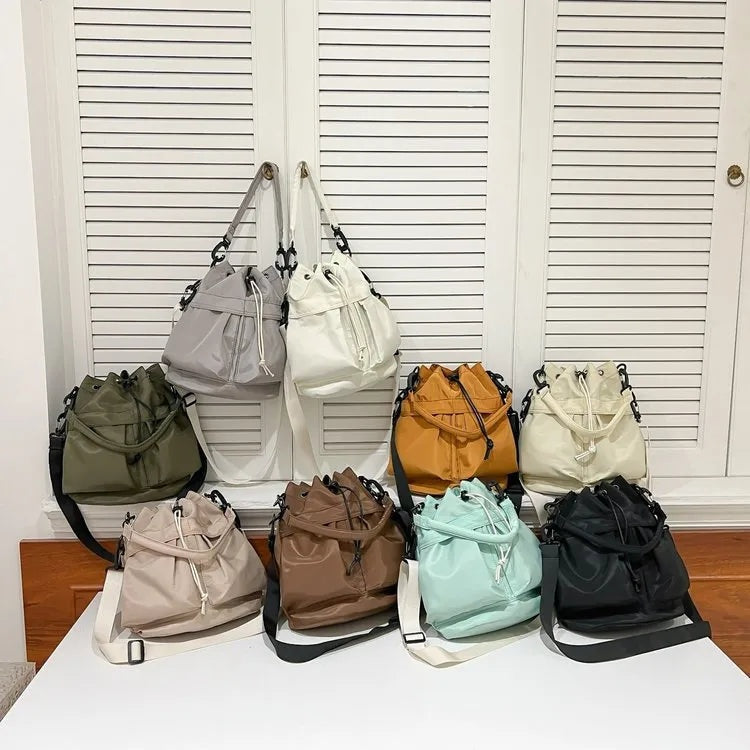 Medium nylon bucket bags in assorted colors feature softly gathered drawstring openings, top handles, structured bases, and detachable side straps.