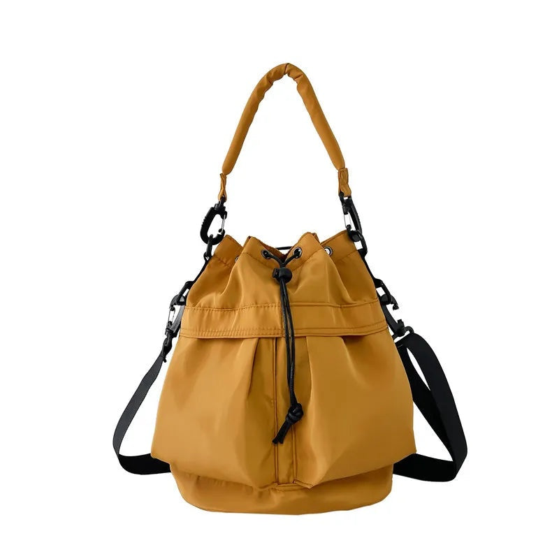Medium mustard-yellow nylon bucket bag with a softly gathered drawstring opening, structured rounded base, top handle, and adjustable side straps with black hardware.