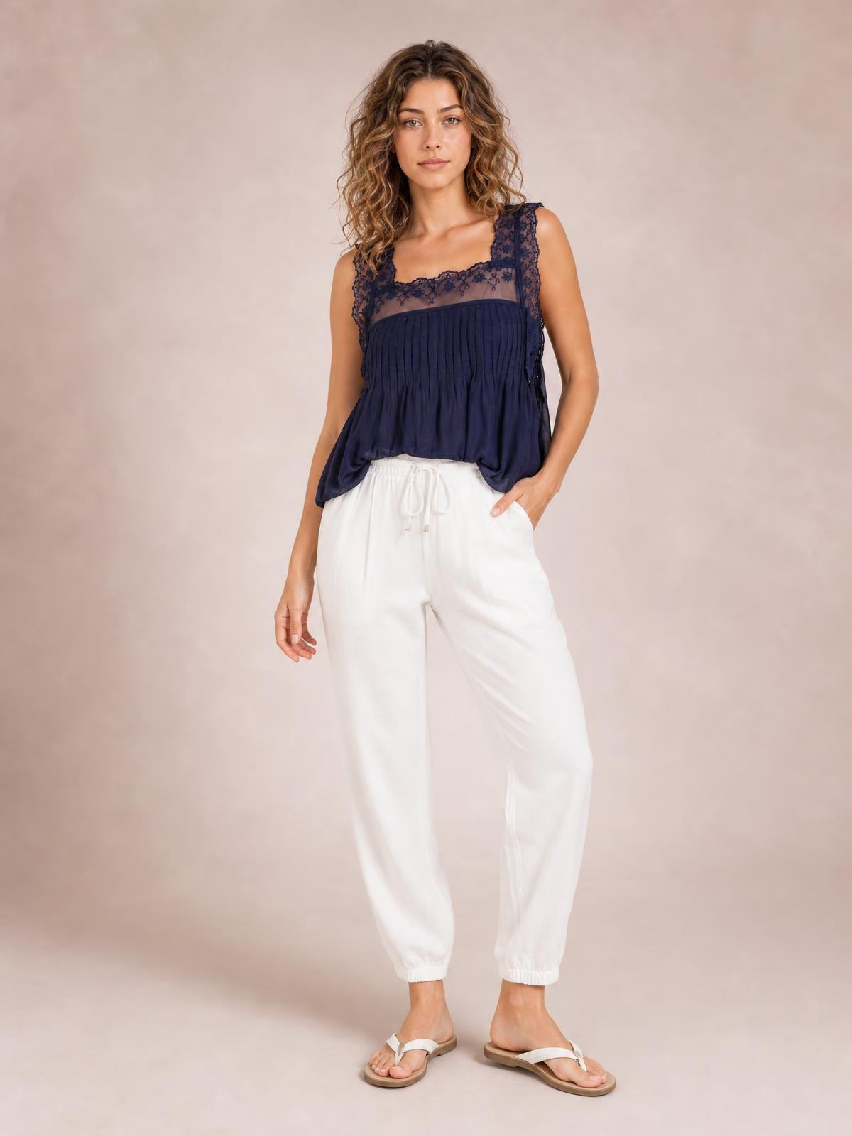 Model stands in white drawstring paperbag waist cropped joggers with a relaxed silhouette, side pockets, and gathered ankle cuffs.