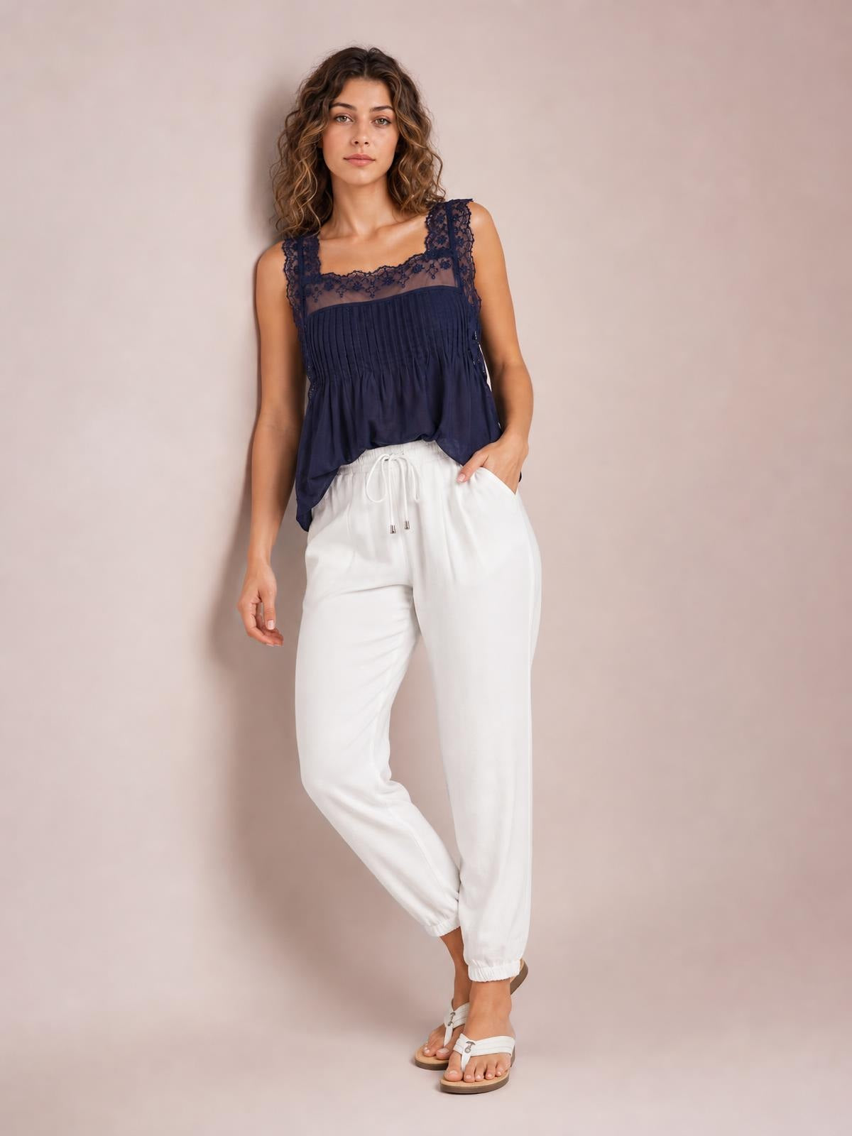 Model wears white drawstring paperbag waist cropped joggers with a relaxed tapered silhouette, elastic cuffs, and one hand tucked into a side pocket.