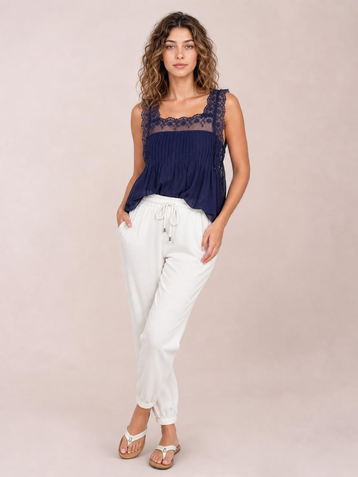 A model poses with one hand in a pocket, wearing white drawstring paperbag waist cropped joggers with a relaxed tapered silhouette and elastic cuffs.