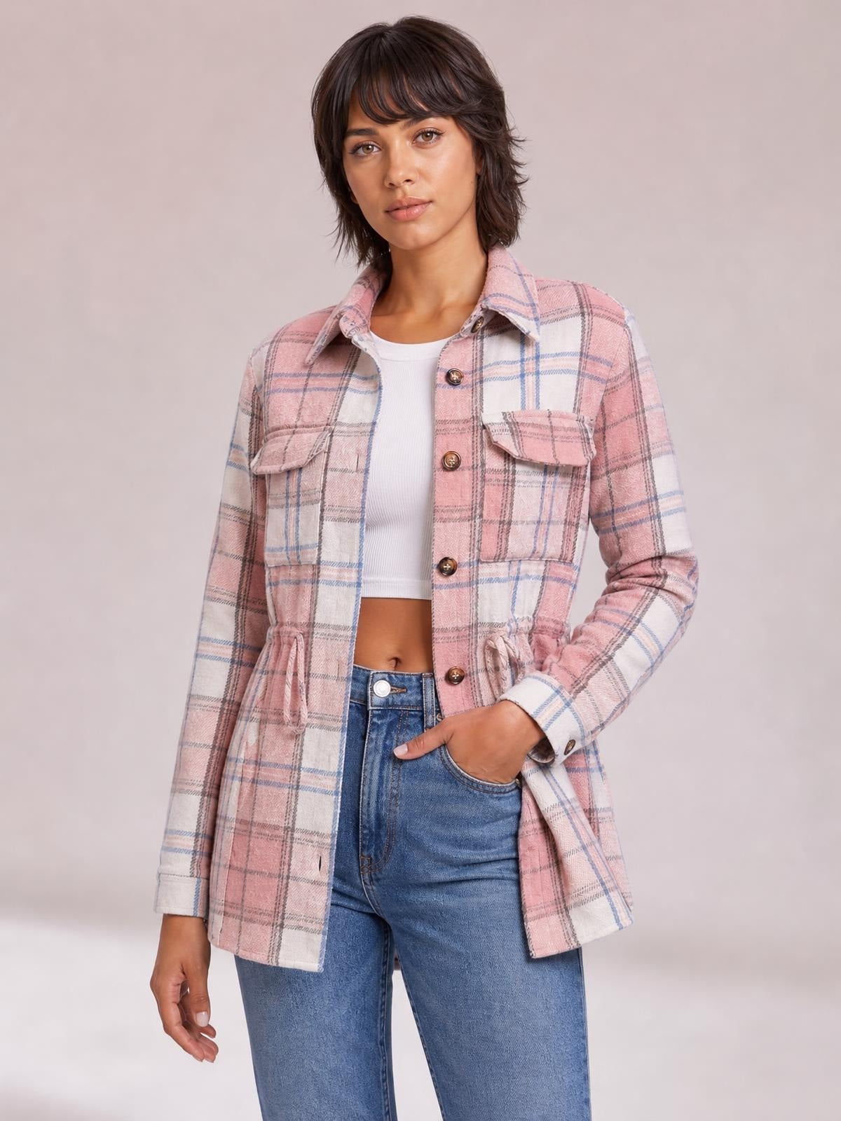 A model wears a pink-and-white plaid button-up jacket with long sleeves, chest flap pockets, a drawstring waist, and a straight silhouette.