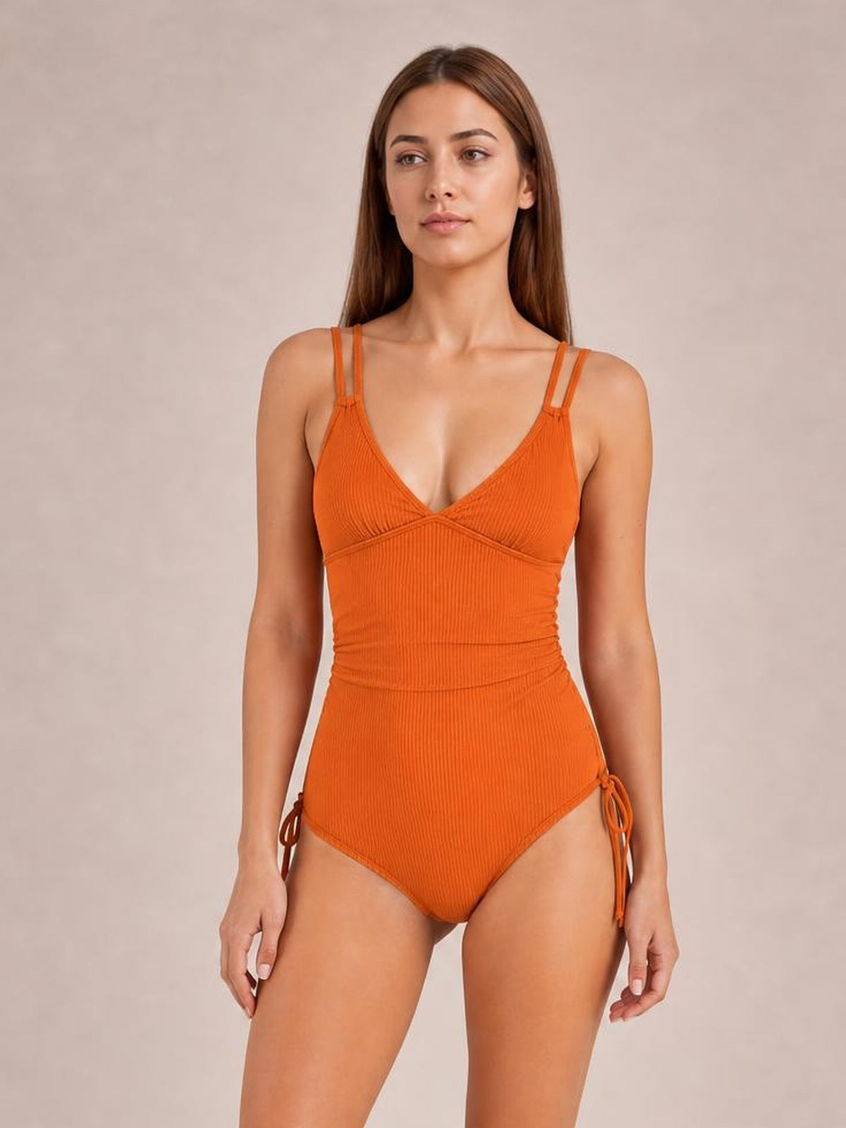 Model stands wearing an orange ribbed drawstring plunge one-piece swimsuit with double shoulder straps, crossover bust construction, and ruched side ties.
