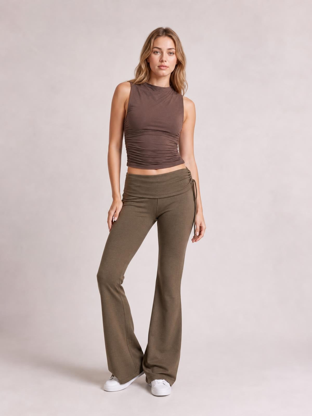 A model stands with one knee bent in taupe drawstring ruched flare pants featuring a high-rise waistband and fitted legs that widen at the hems.