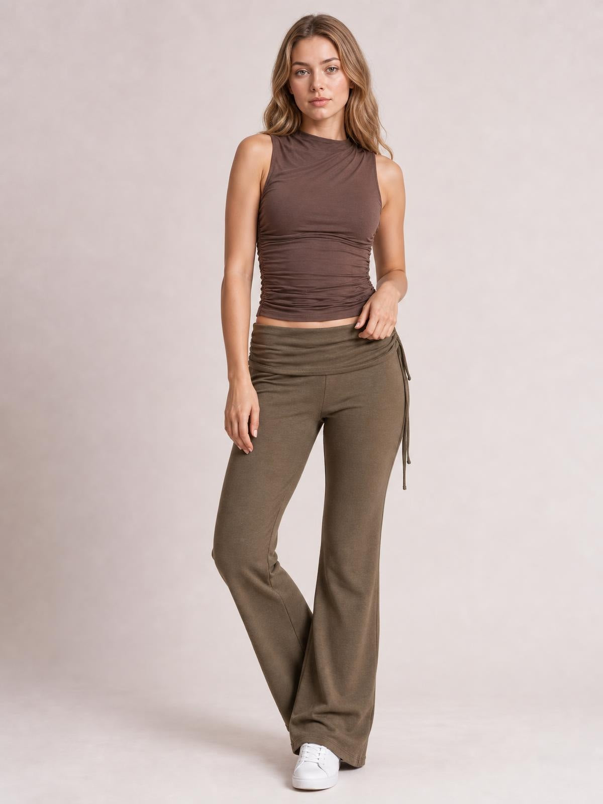 Model stands with one leg crossed, wearing olive-brown drawstring ruched flare pants with a wide-leg silhouette and gathered waistband.