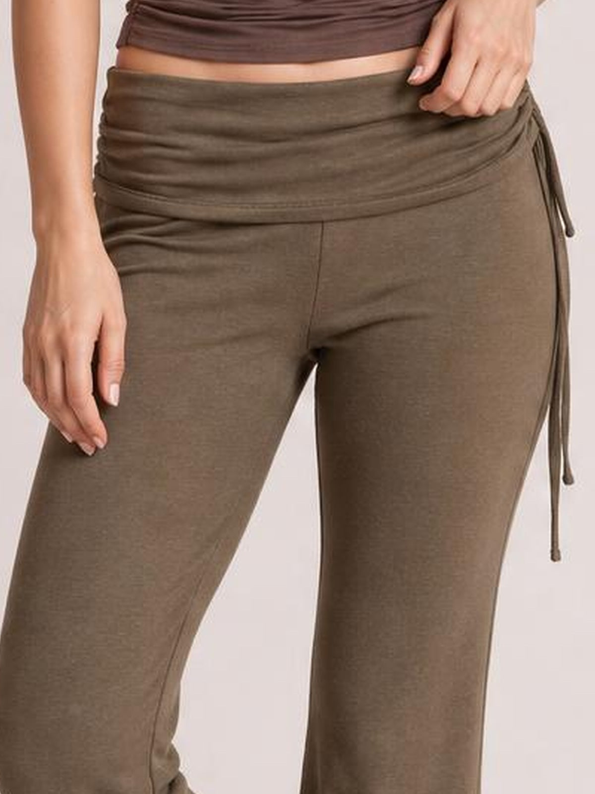Model wears brown drawstring ruched flare pants with a fitted silhouette, gathered waistband, side tie, and visible seam construction.