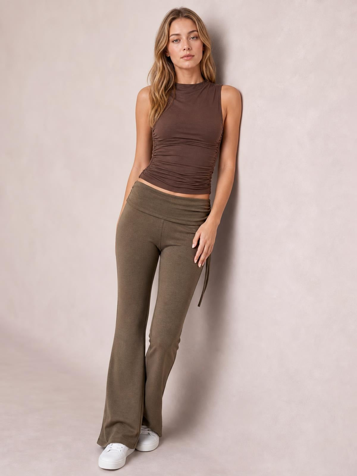 A model poses in olive-brown drawstring ruched flare pants with a wide waistband, fitted legs, and softly flared hems.
