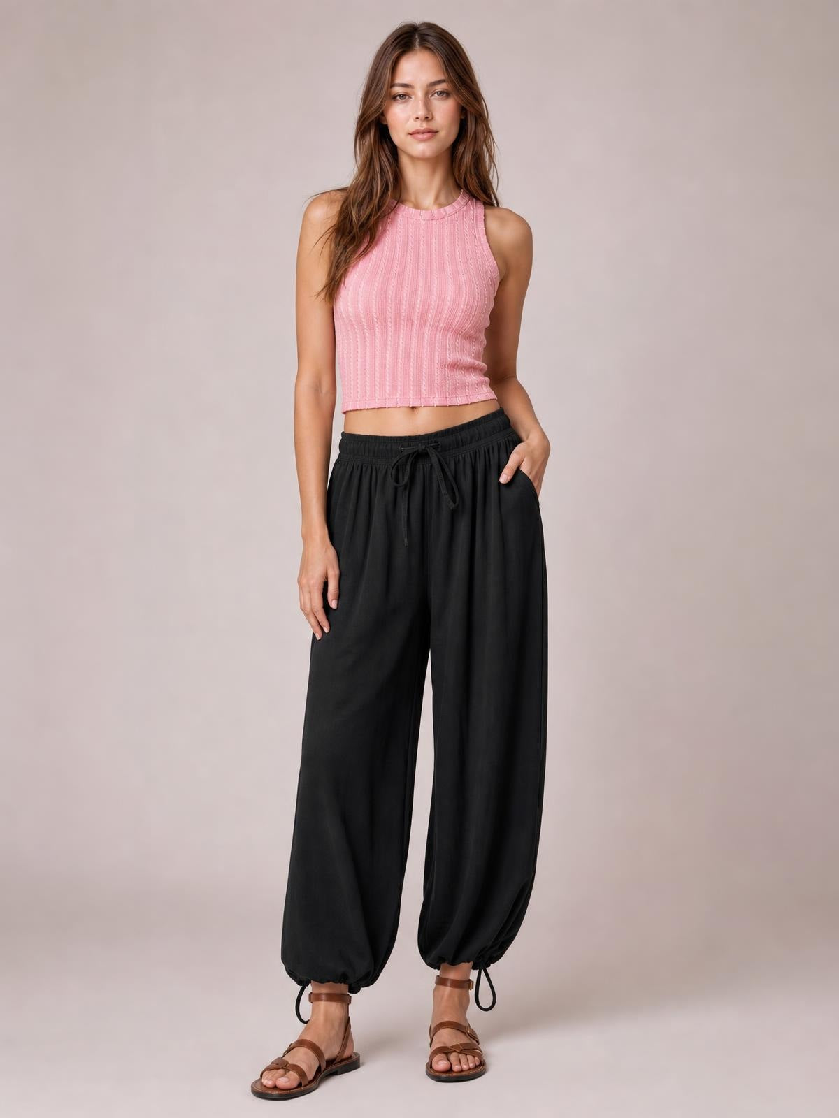 Model stands in black drawstring ruched pants with an elastic waist, relaxed wide-leg silhouette, and gathered ankle cuffs.