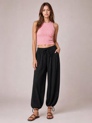 Model stands in black drawstring ruched pants with an elastic waist, relaxed wide-leg silhouette, and gathered ankle cuffs.