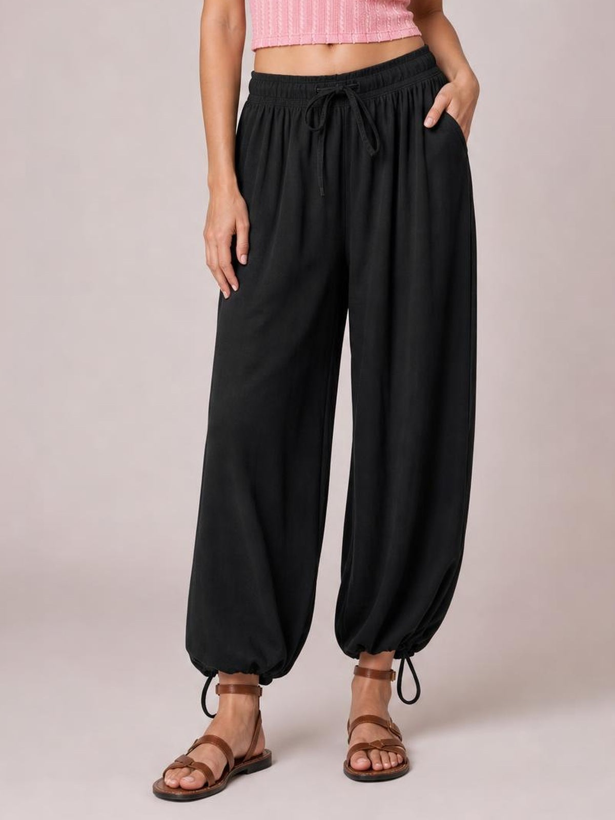 A model poses in black drawstring ruched pants with a relaxed wide-leg silhouette, elastic waist, gathered cuffs, and side pockets.