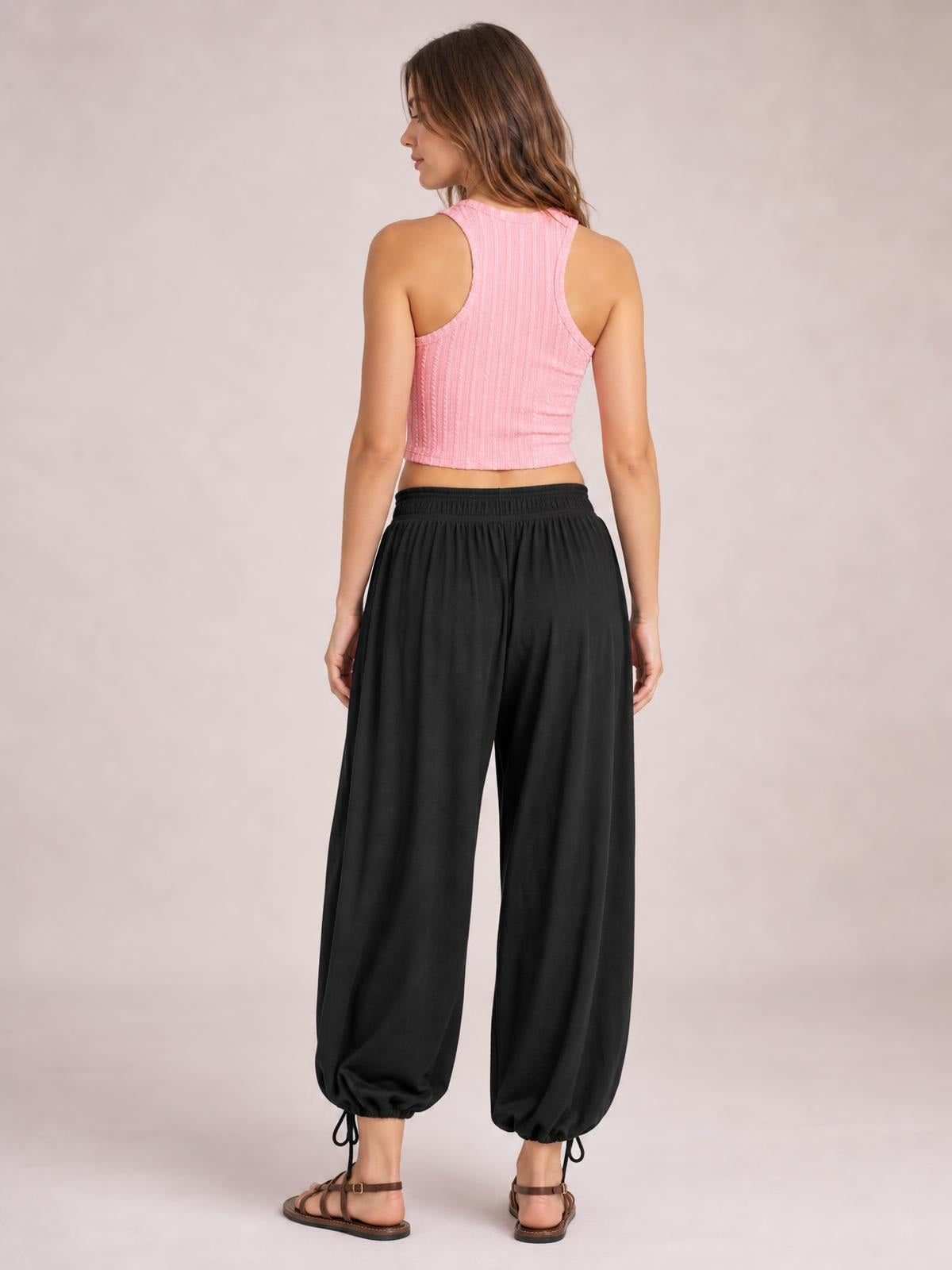Model shown from the back wearing black drawstring ruched pants with a relaxed wide-leg silhouette and gathered ankle cuffs.