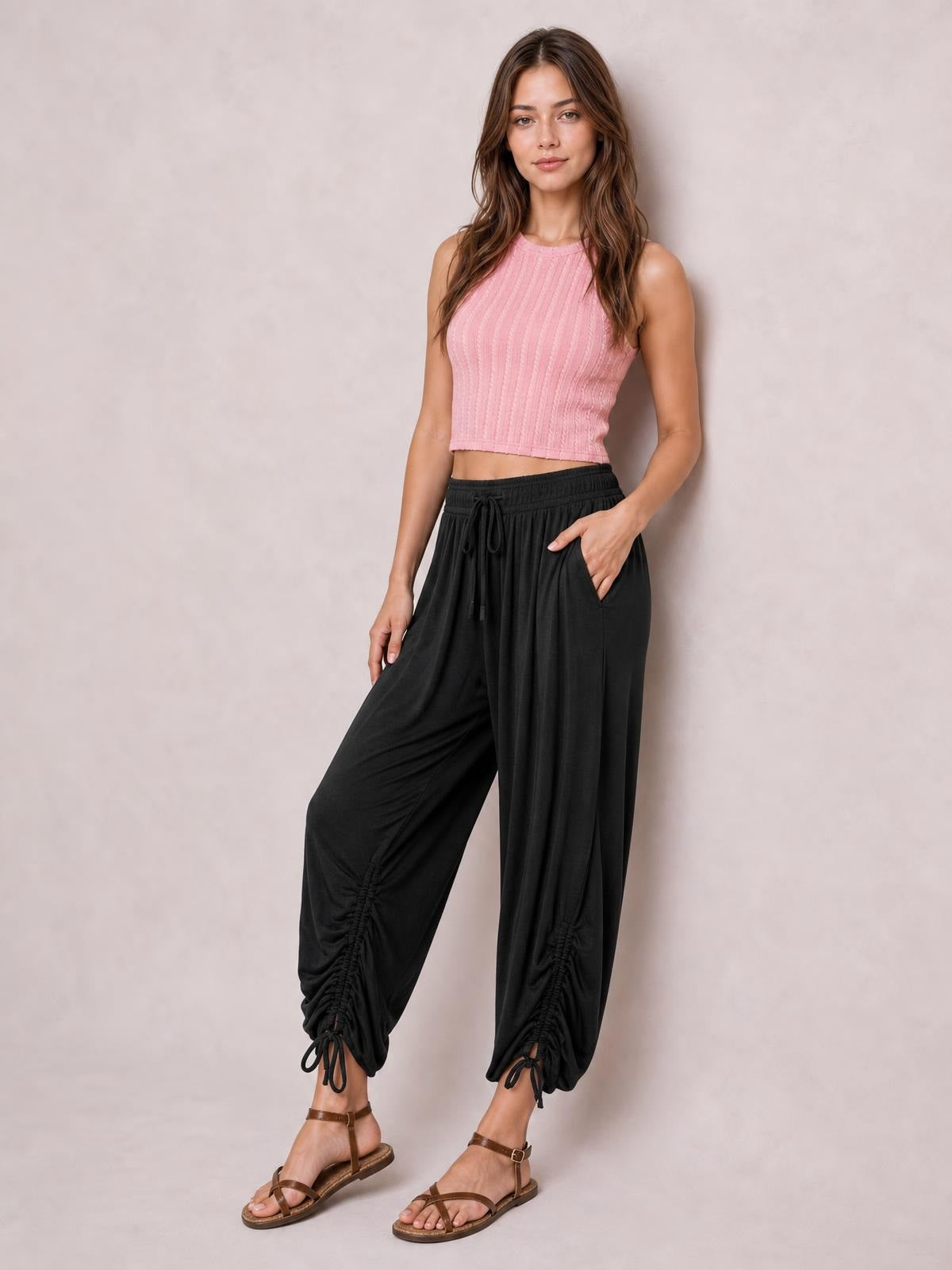 A model stands in black drawstring ruched pants with a relaxed wide-leg silhouette, elastic waist, side pockets, and gathered ankle hems.