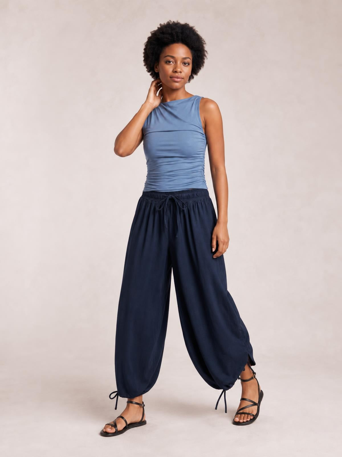 Model poses in navy blue drawstring ruched pants with a relaxed wide-leg silhouette, elastic waist, and adjustable ankle ties.
