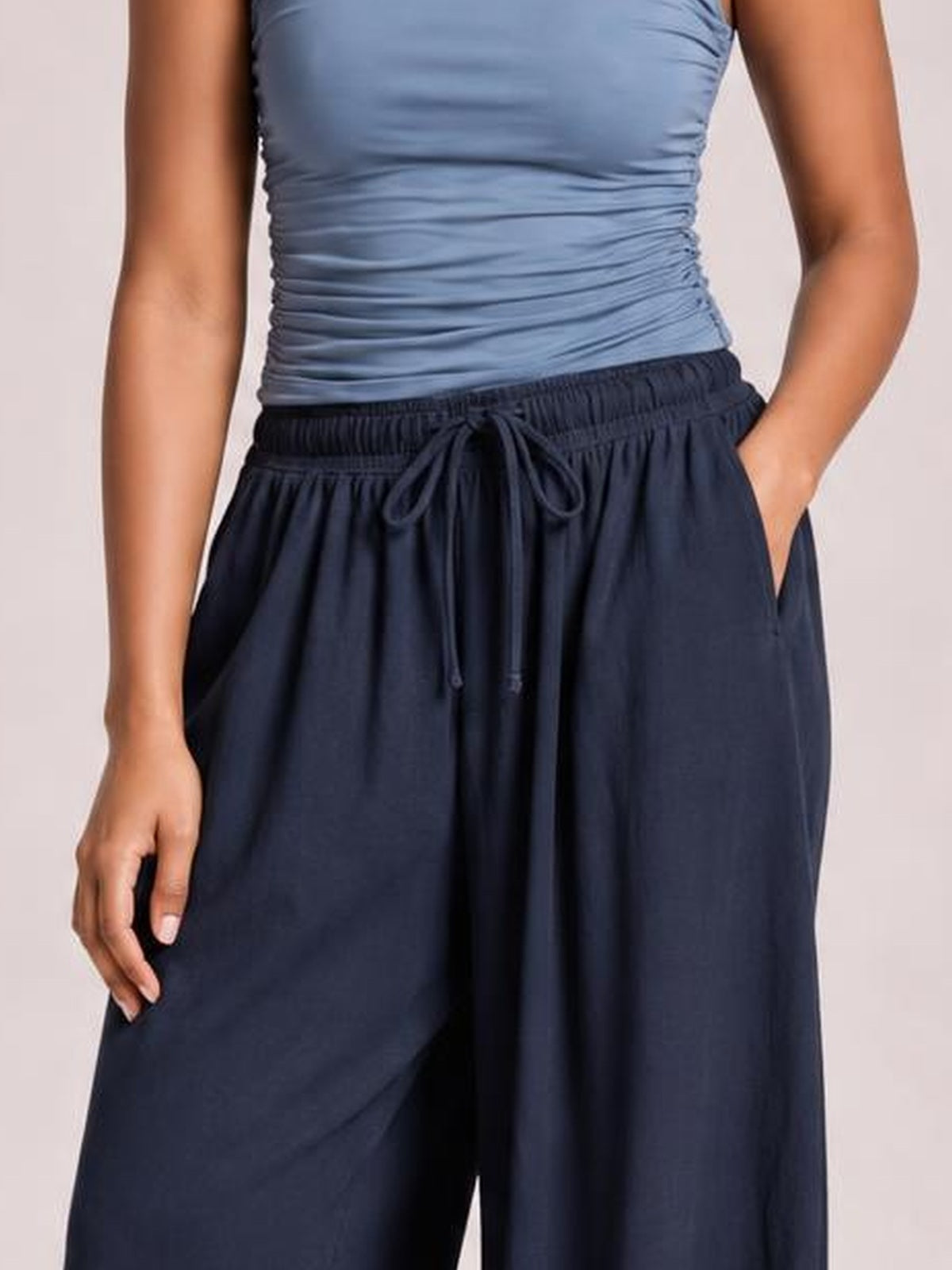 Model wearing dark navy Drawstring Ruched Pants with a wide-leg silhouette, elastic waistband, visible tie, and side pockets, standing with one hand in a pocket.