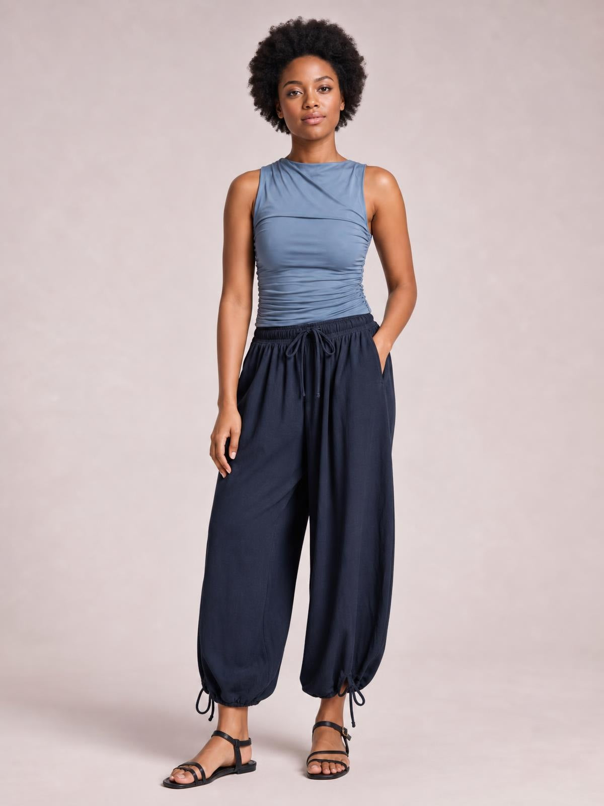 A model stands with one hand in a pocket, wearing opaque navy drawstring ruched pants with a relaxed wide-leg silhouette and gathered ankle hems.