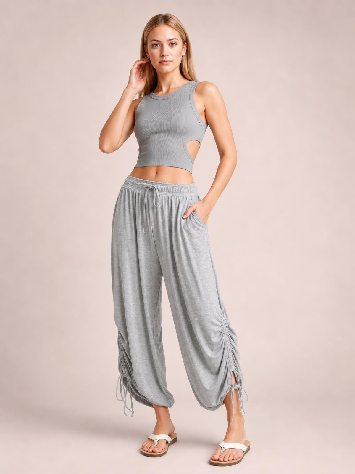 Model poses in light gray drawstring ruched pants with a relaxed wide-leg silhouette, gathered hems, and side pockets.