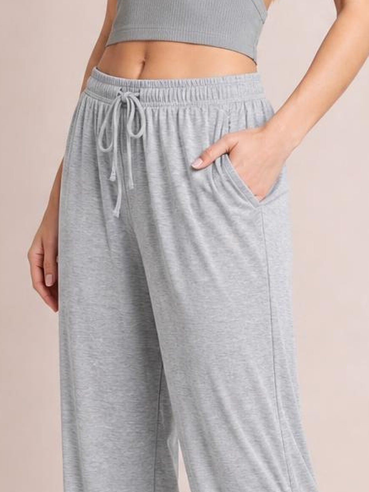 Model wears light gray ruched pants with a relaxed wide-leg silhouette, elastic drawstring waist, and side pockets, posing with one hand tucked inside.