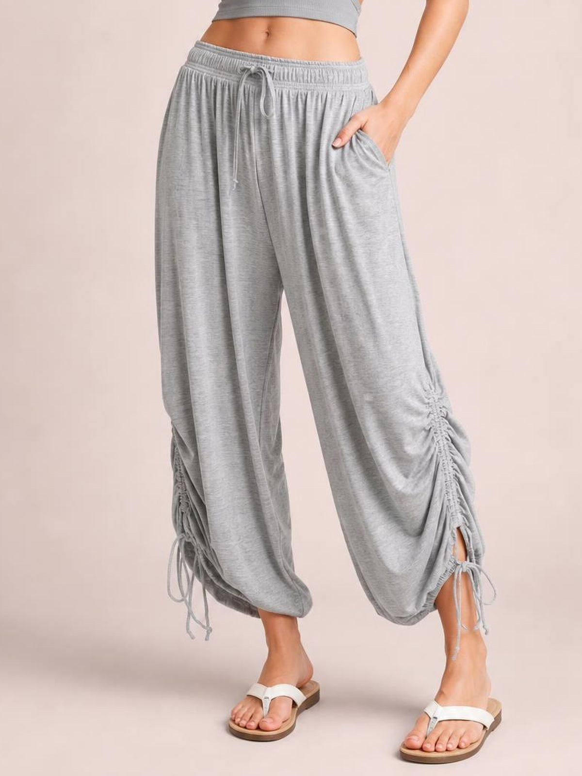 Model wearing gray Drawstring Ruched Pants with an elastic waist, wide-leg silhouette, side pockets, and ruched ankle hems with adjustable ties.