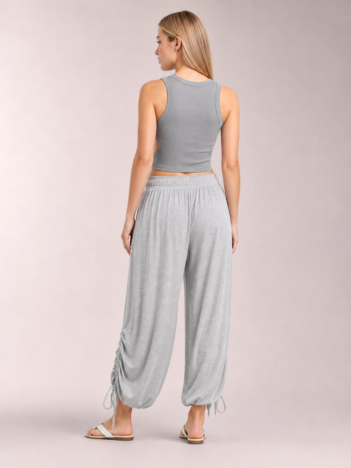 Model shown from the back wears light gray drawstring ruched pants with an elastic waist, wide legs, and gathered ankle hems.