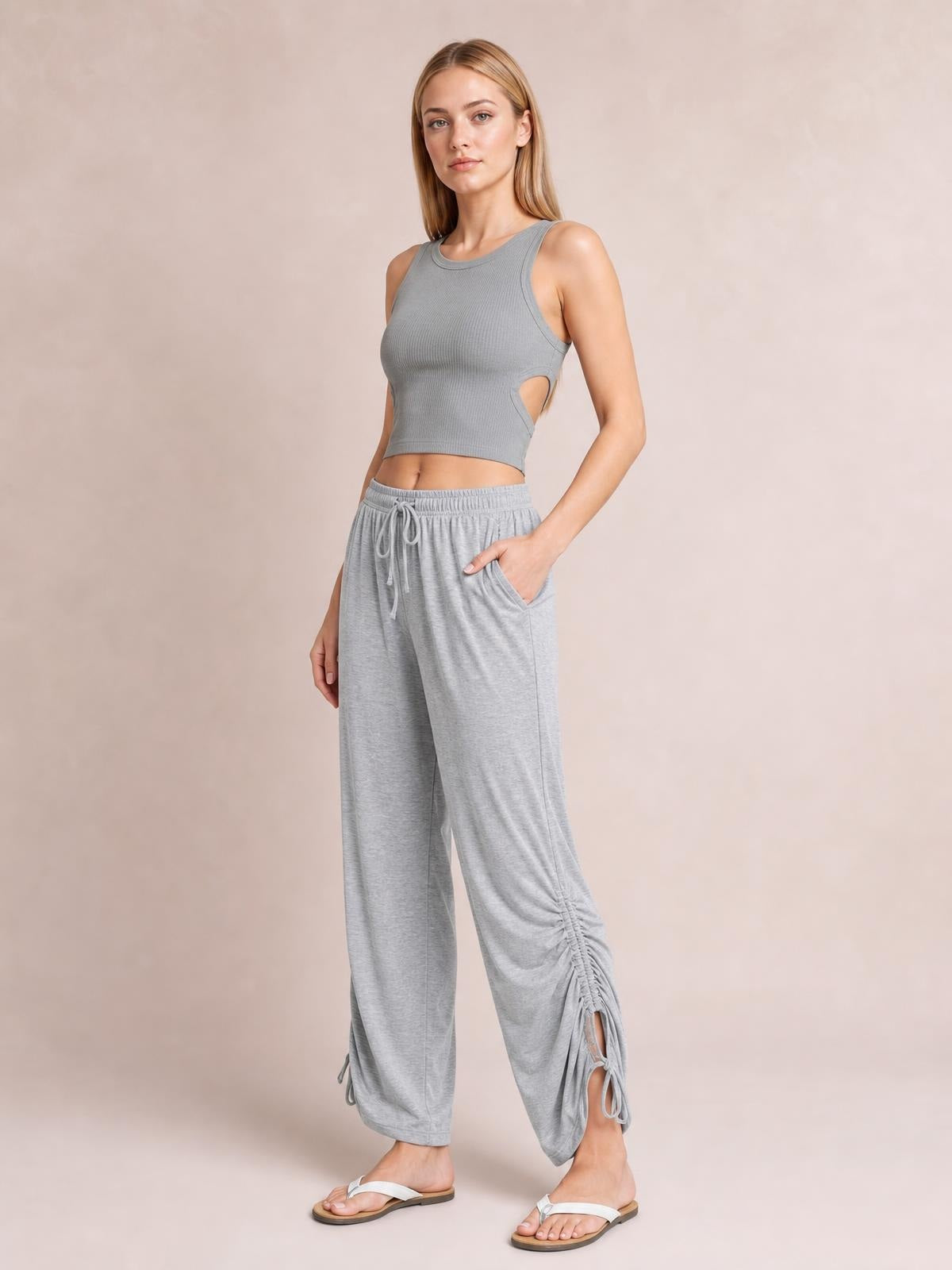 A woman models light gray drawstring ruched pants with a relaxed wide-leg silhouette, elastic waistband, side pockets, and gathered ankle details.