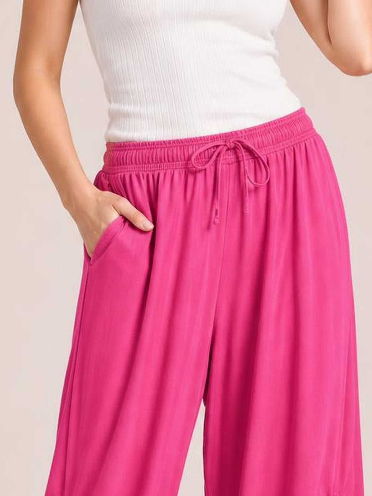 Model wears bright pink drawstring ruched pants with a wide-leg silhouette, elastic waistband, front tie, and side pockets, posed with one hand tucked in.