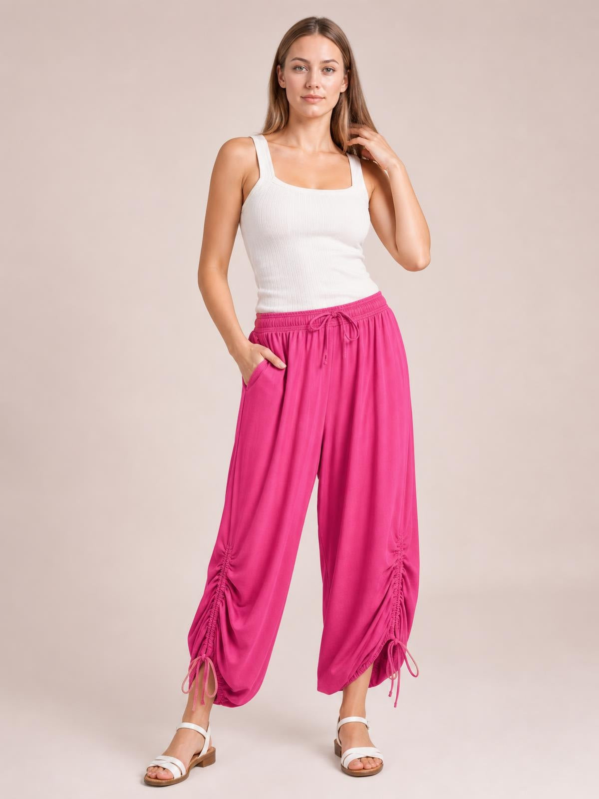 Model poses in bright pink drawstring ruched pants with a relaxed wide-leg silhouette, gathered ankle details, side pockets, and an elastic waistband.