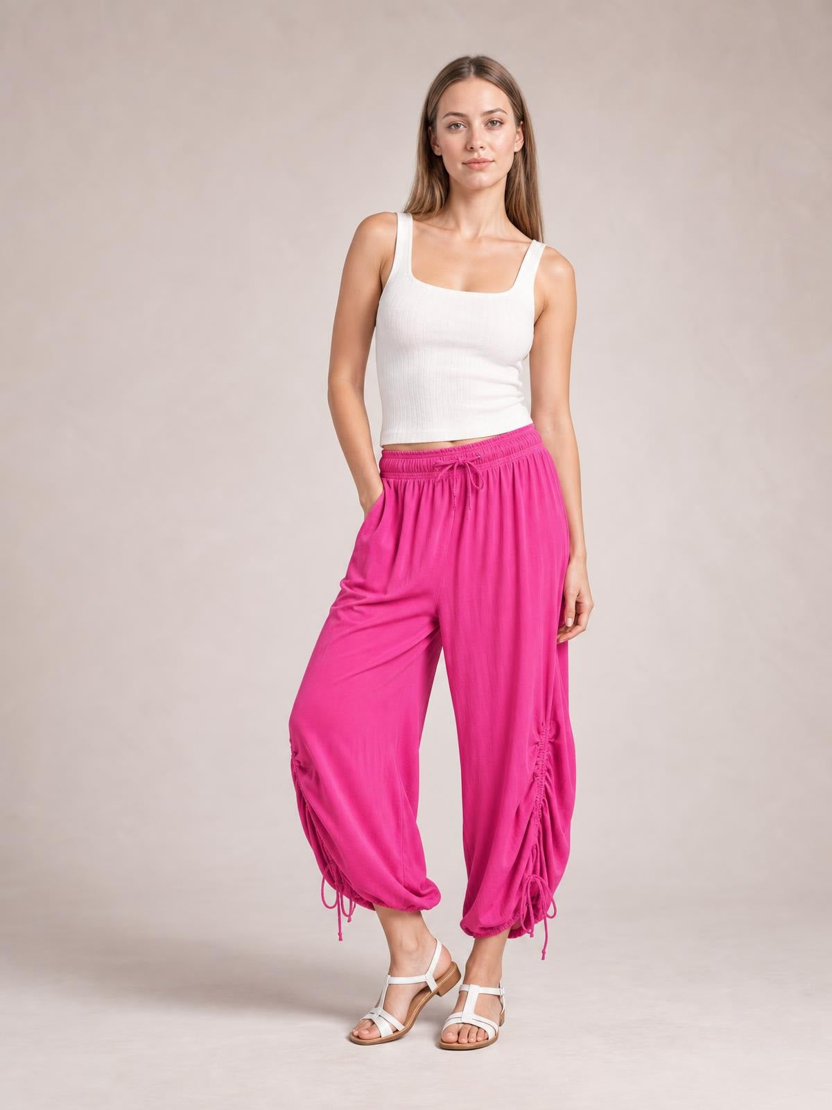 A model poses with one hand in a pocket, wearing bright pink drawstring ruched pants with a relaxed wide-leg silhouette, elastic waist, and gathered ankle hems.
