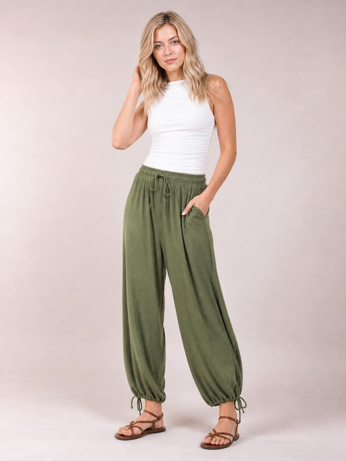 Model poses in olive-green ruched pants with a drawstring elastic waist, relaxed wide legs, ankle cuffs, and side pockets.