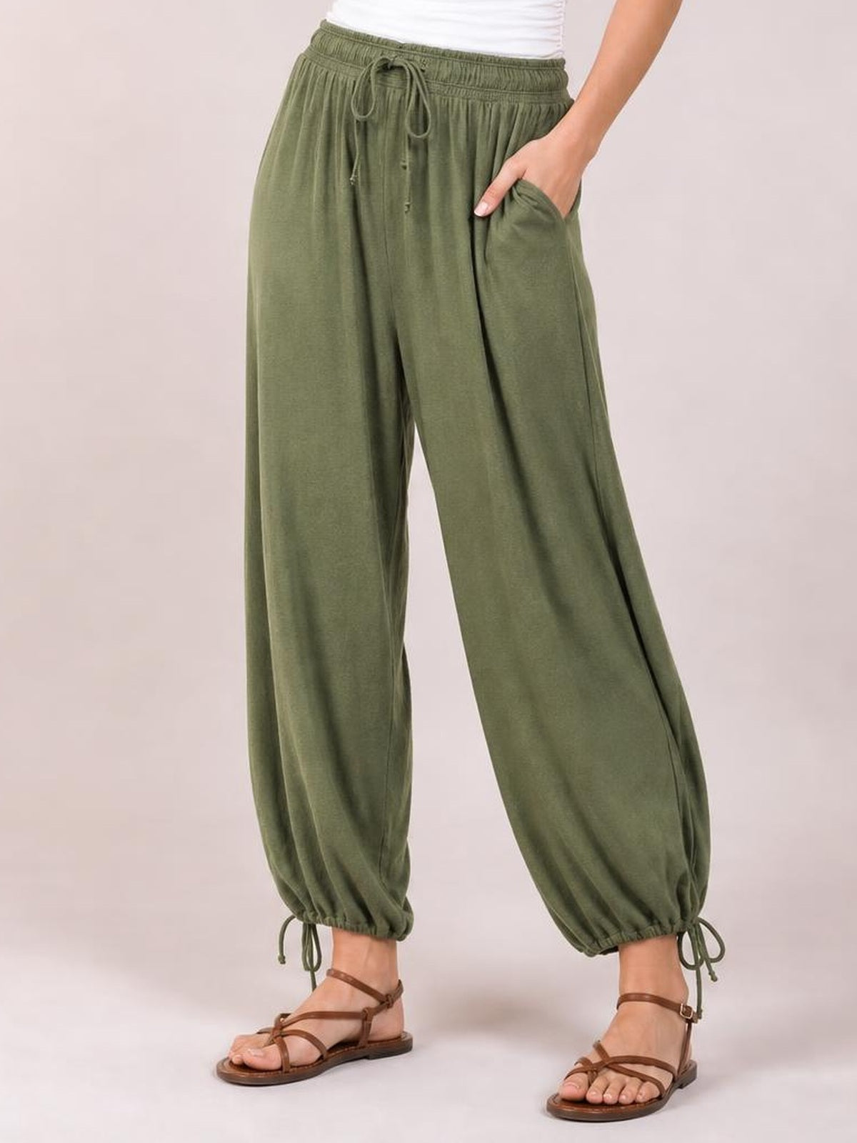 Model wearing olive green drawstring ruched pants with a relaxed wide-leg silhouette, elastic waist, side pockets, and adjustable gathered ankle hems.