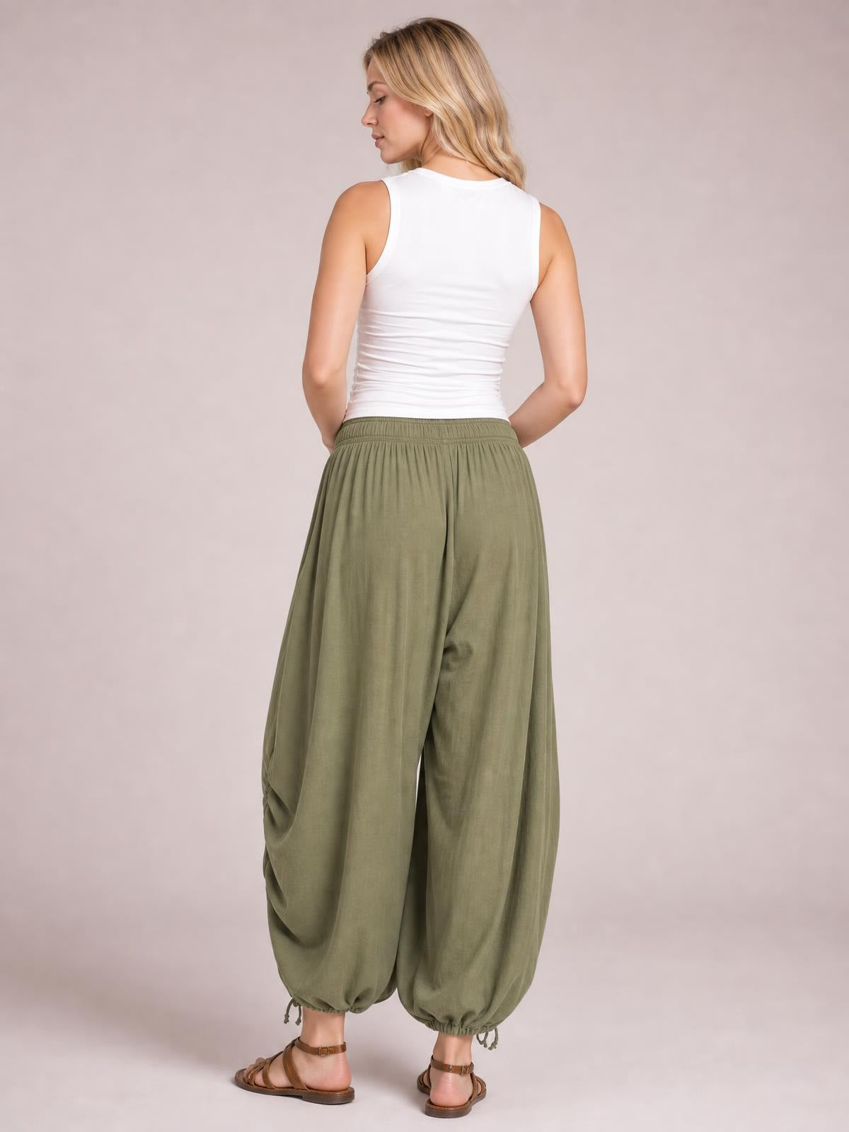 A model shown from behind wears olive green drawstring ruched pants with a relaxed balloon silhouette, elastic waist, gathered side details, and drawstring cuffs.