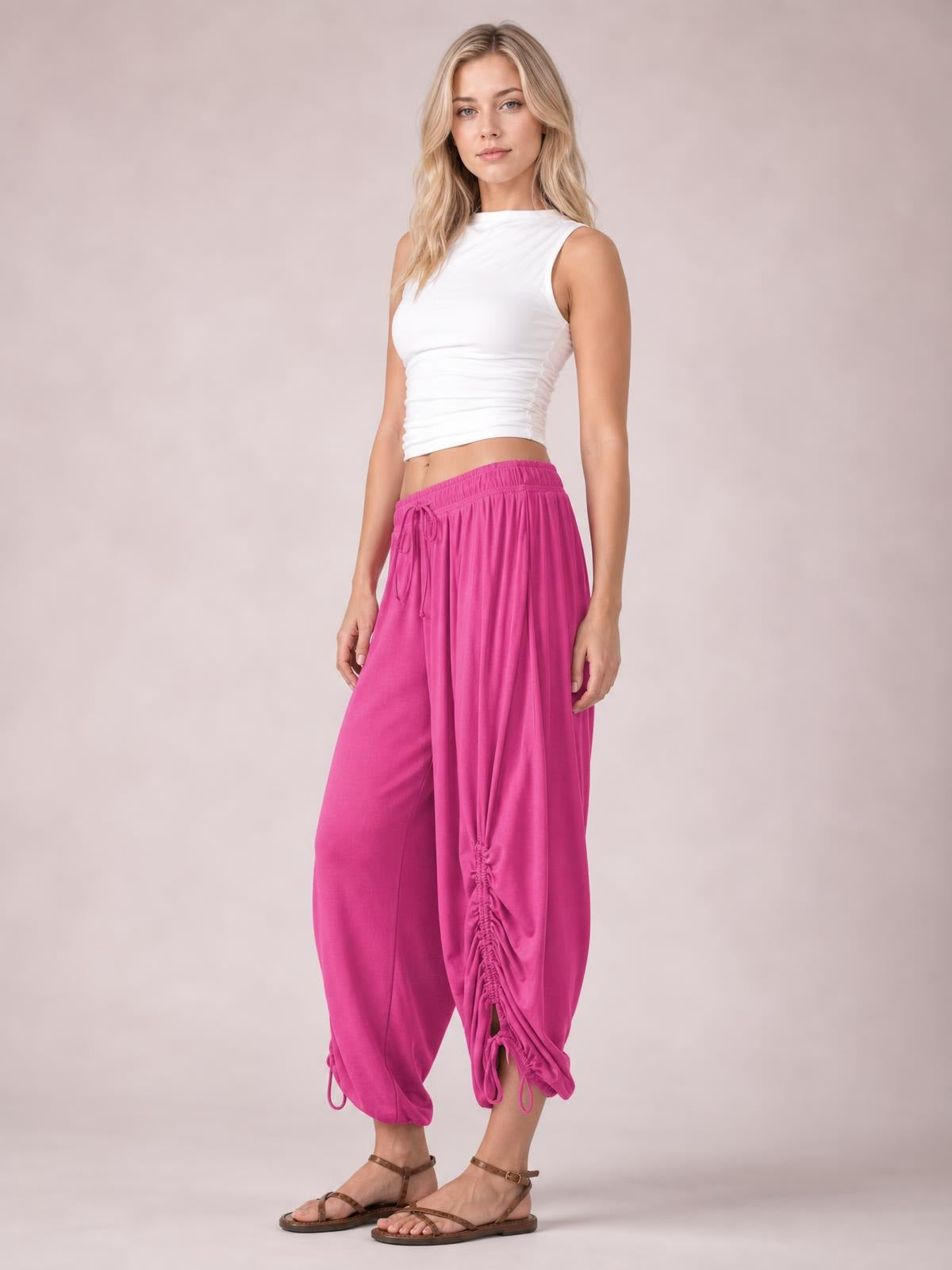 Model poses in bright pink drawstring ruched pants with a relaxed cropped silhouette, elastic waistband, and gathered ankle details.