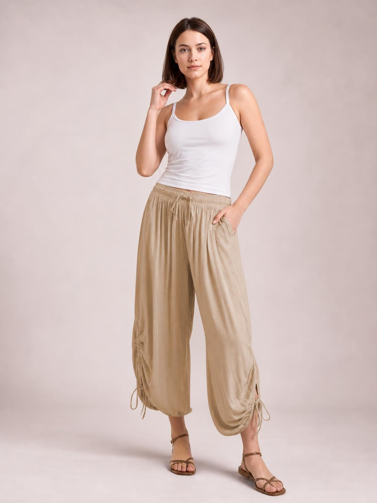 Model poses in beige drawstring ruched pants with a relaxed wide-leg silhouette, gathered ankle hems, and hands tucked into side pockets.