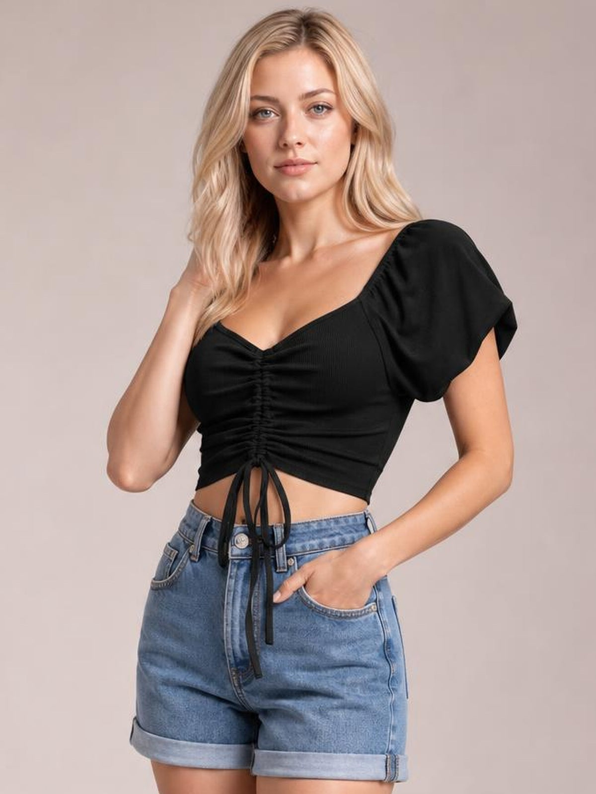 Model poses in a black drawstring short sleeve crop top with ruched center detailing, a cropped silhouette, and gently puffed sleeves.