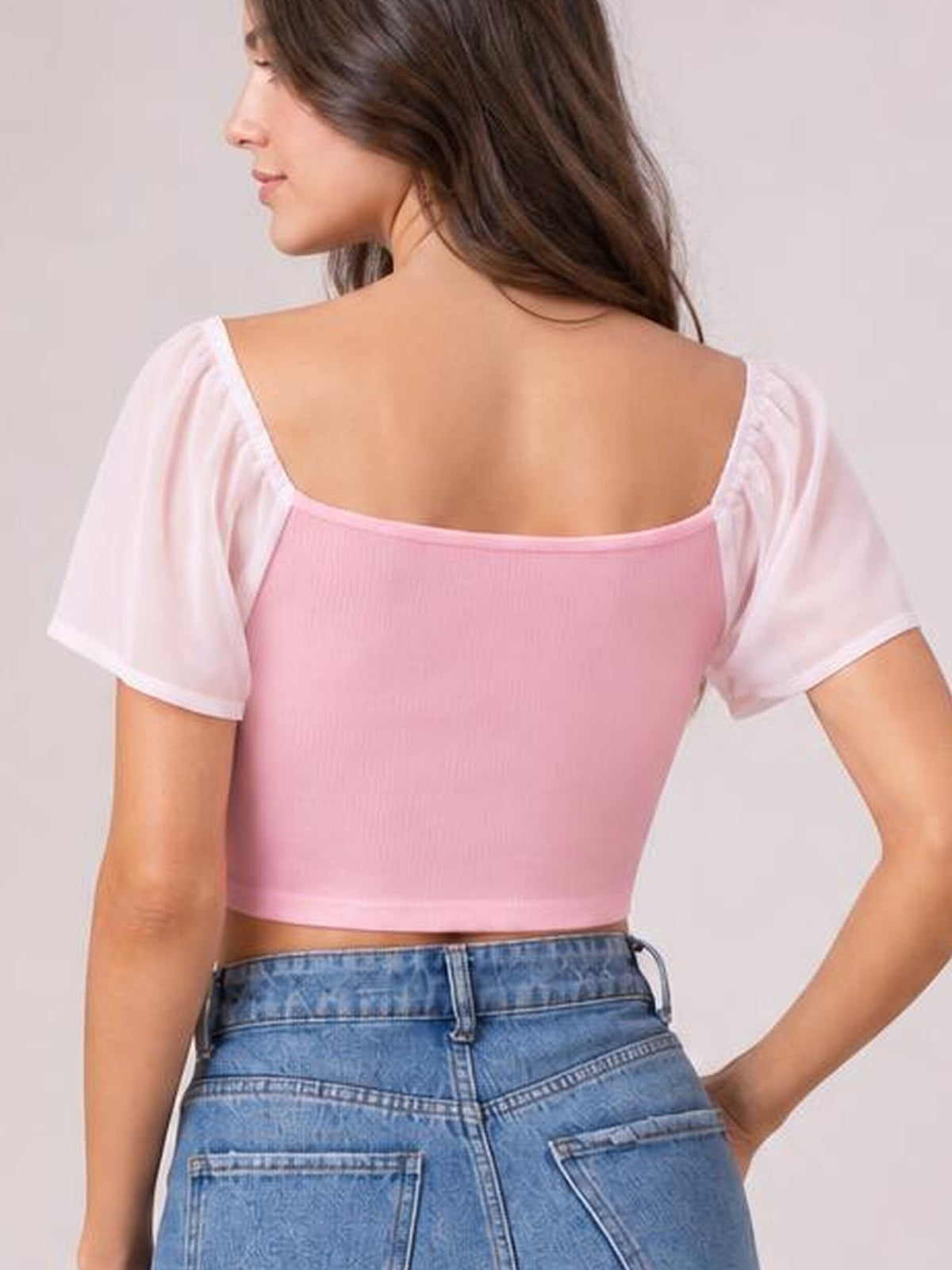A model turns to show a pink drawstring crop top with short sleeves, a wide scoop back, fitted silhouette, and exposed midriff.