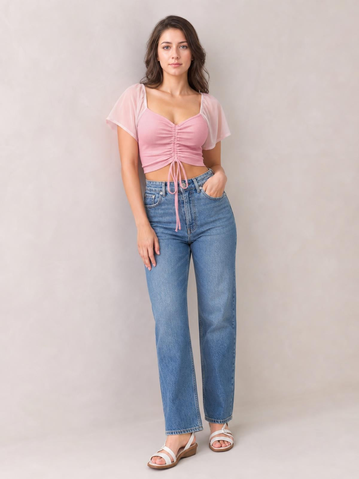 Model poses with one hand in her pocket wearing a pink drawstring short sleeve crop top with ruched front detailing and a fitted silhouette.