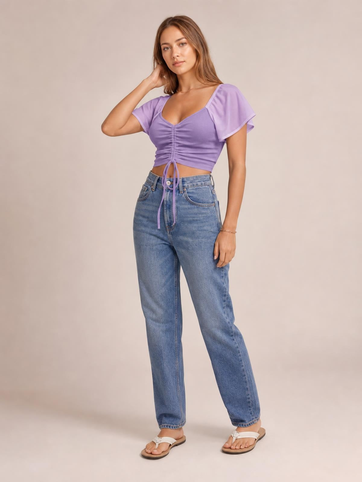 Model wears a lavender drawstring short sleeve crop top with a fitted silhouette, ruched center front, and flutter sleeves, posing with one hand in her hair.
