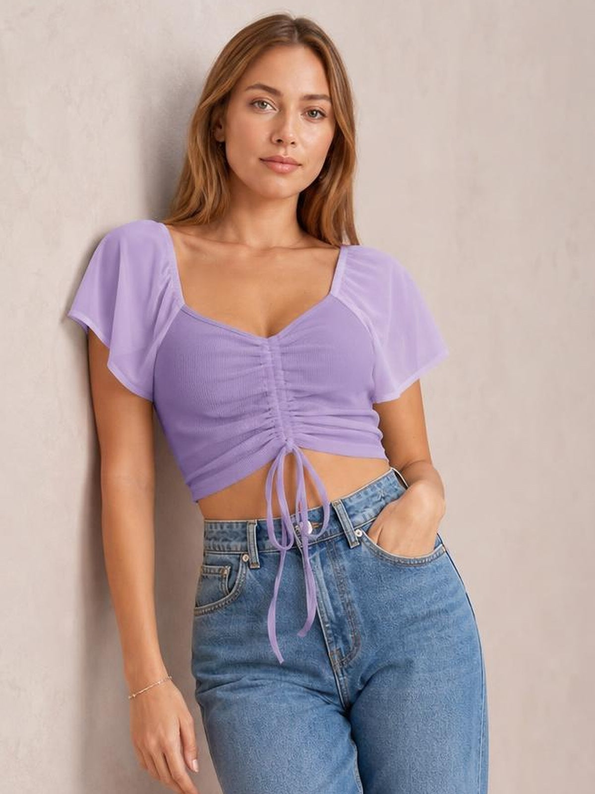 Model poses in a lavender drawstring short sleeve crop top with a ruched center, tie-front detail, sweetheart neckline, and fitted silhouette.